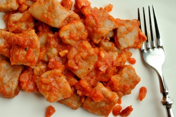 overhead view of gnocchi in a tomato, onion, and pancetta sauce on a white plate