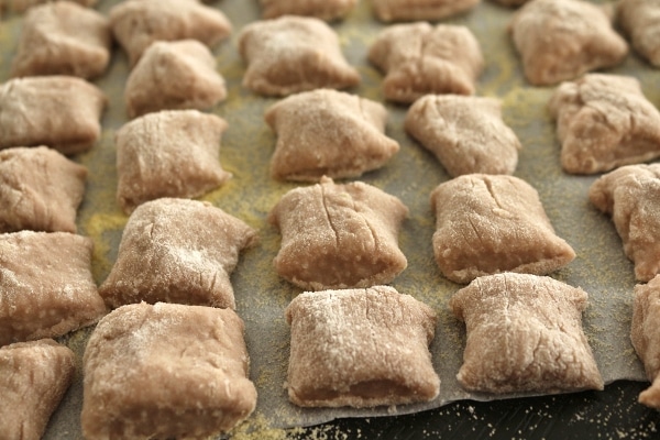 A closeup of wine-infused gnocchi squares on a cornmeal dusted tray