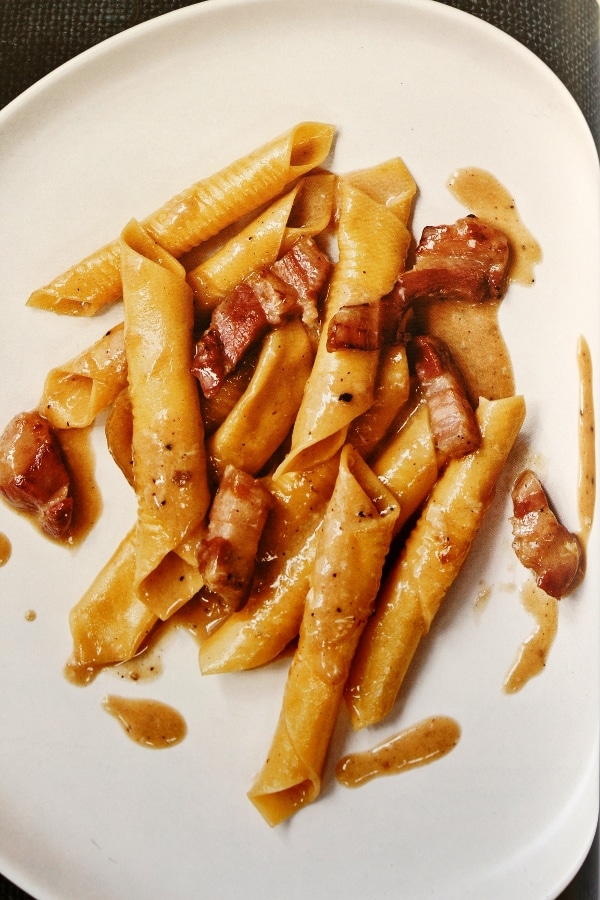 overhead view of garganelli pasta with bacon on a white plate