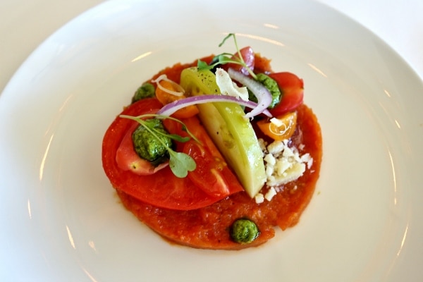 A plate of fresh vegetables including heirloom tomatoes with dollops of pesto