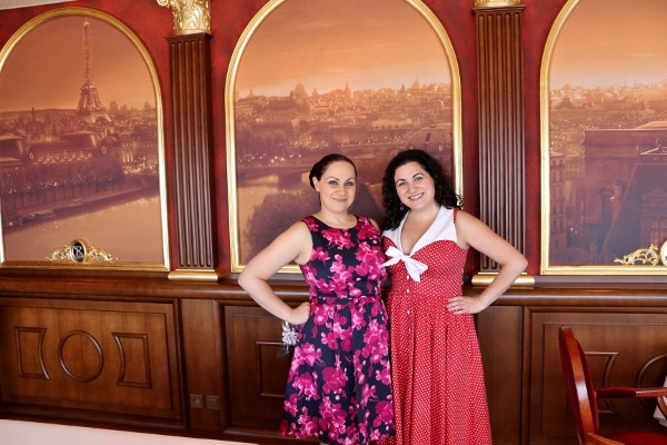 two women posing in front of a painting of Paris