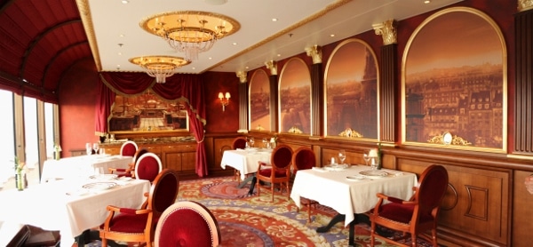 a very posh looking dining room with an ornate carpet and wall painting of Paris