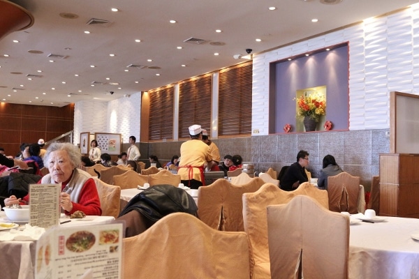 a large restaurant dining room with people pushing dim sum carts between tables