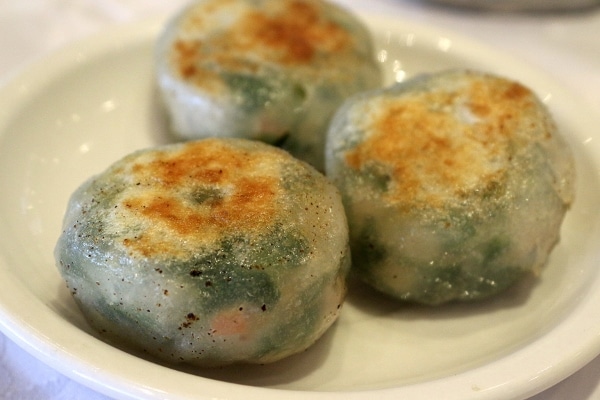 A plate of pan-fried dumplings with green filling showing through the wrapper