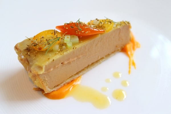 a closeup of a slice of foie gras tart topped with candied orange