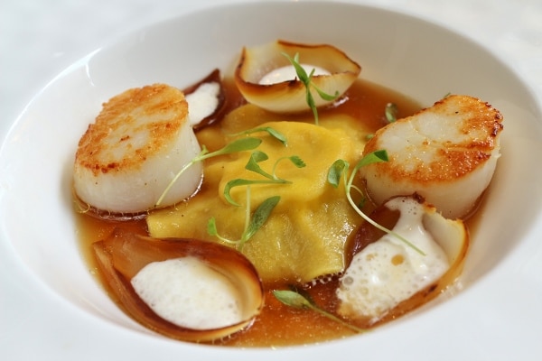 a big ravioli in brown broth served with seared scallops and charred onions