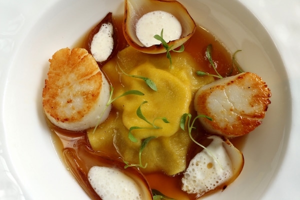 overhead view of a big ravioli in brown broth served with seared scallops