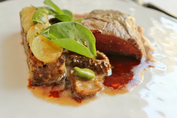 a closeup of a terrine topped with discs of potato, served with roasted beef