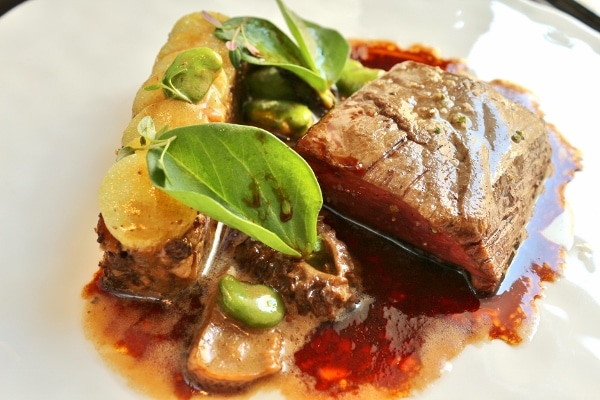 A closeup of a piece of roasted beef with a dark brown sauce and herbs on top