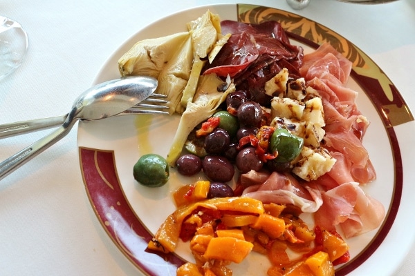 A plate of antipasti including cured meats, cheese, olives, and vegetables