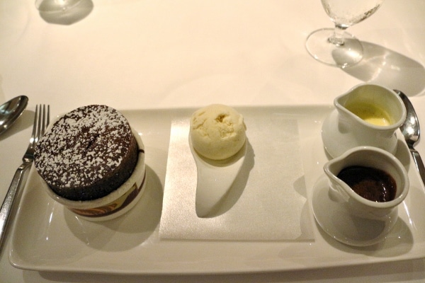 a chocolate souffle served with a scoop of ice cream and two sauces