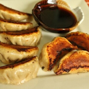 closeup of a plate of pan-fried pork and chive dumplings with dipping sauce