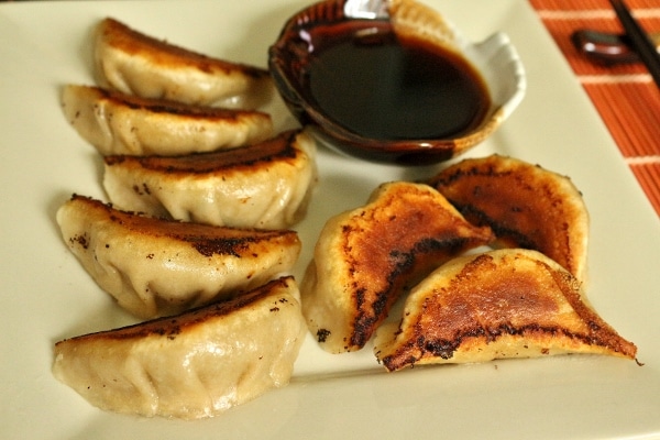 closeup of a plate of pan-fried pork and chive dumplings with dipping sauce