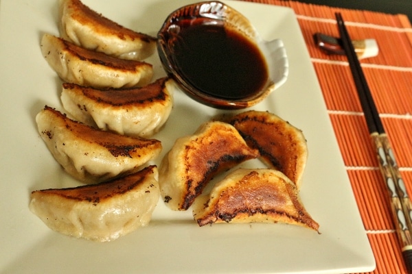 A plate of pan-fried pork and chive dumplings with dipping sauce