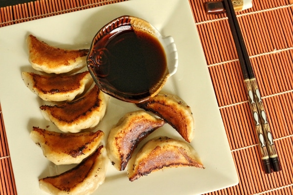overhead view of a plate of pan-fried pork and chive dumplings with dipping sauce