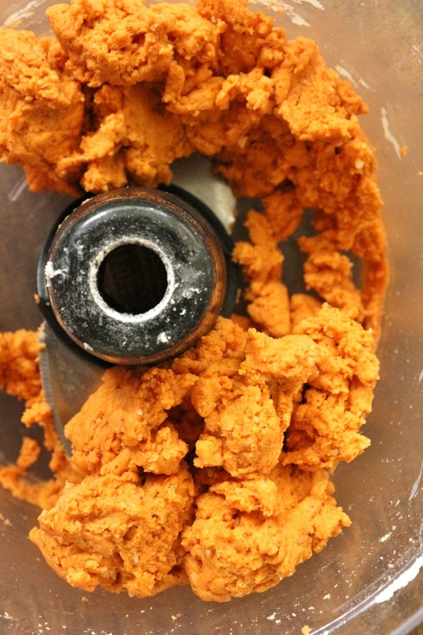 A closeup of cheddar cheese cracker dough in the bowl of a food processor