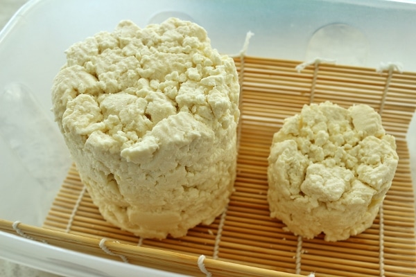 a side view of a large and small wheel of unaged cheese on a sushi mat