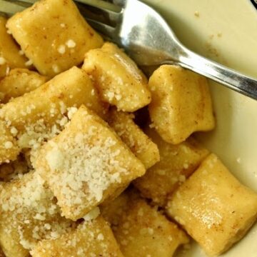 a closeup of a bowl of dunderi gnocchi in brown butter topped with grated cheese