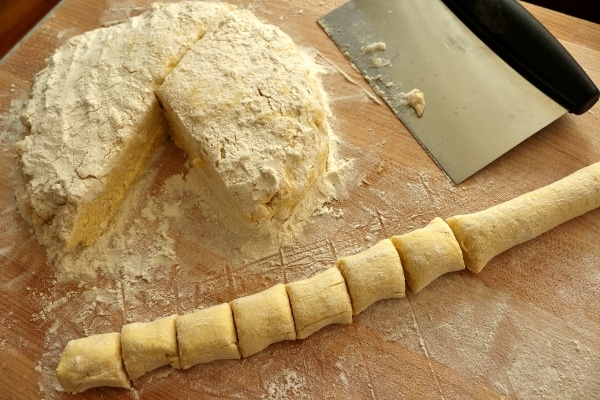 a pile of dough and a bunch of cut gnocchi on a wooden board