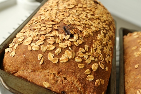 a loaf of oat-topped bread in a metal pan