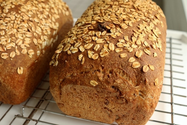 two loaves of whole wheat bread topped with oats on cooling racks