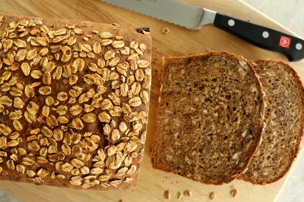 overhead view of a half-sliced loaf of whole wheat sandwich bread topped with oats