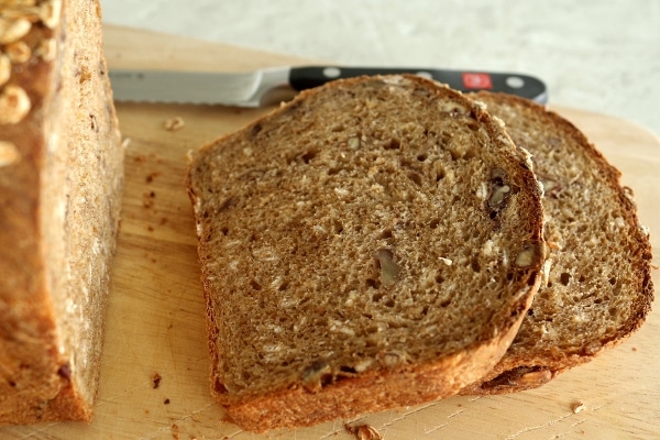 a closeup of slices of whole wheat bread with oats and pecans on a wooden board