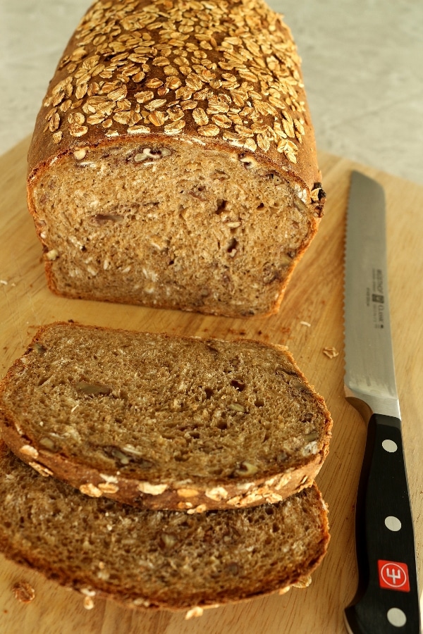 a half-sliced loaf of whole wheat sandwich bread with oats on a wooden board