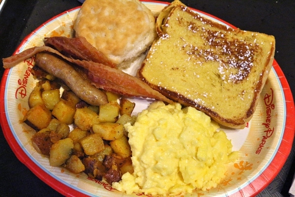 A plate of scrambled eggs, home fries, breakfast meats, french toast, and a biscuit