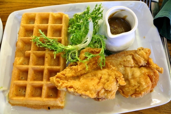 a plate of chicken and waffles served with a small pitcher of sauce