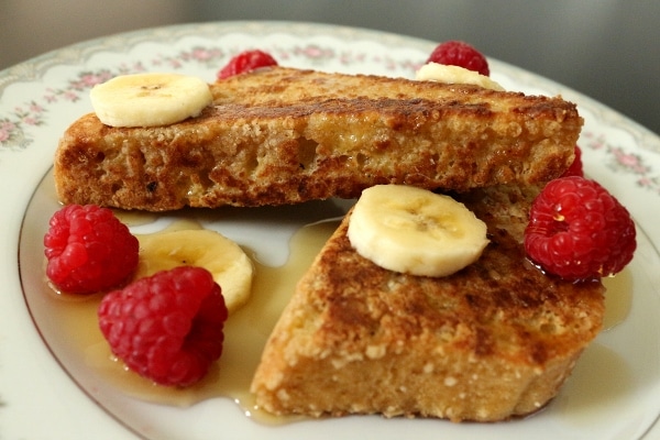 closeup of french toast on a plate with whole raspberries and sliced banana