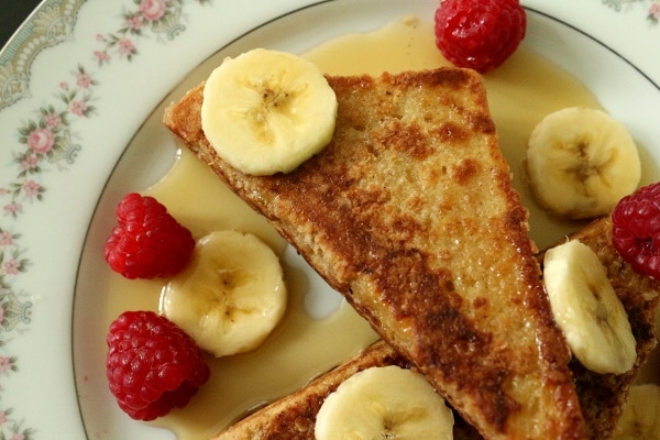 overhead closeup of french toast on a plate with sliced bananas and raspberries