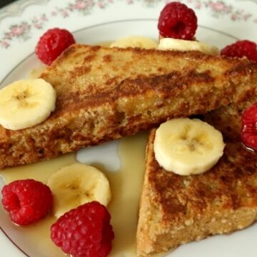 two triangles of french toast on a plate with raspberries and bananas