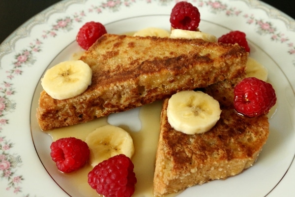 two triangles of french toast on a plate with raspberries and bananas