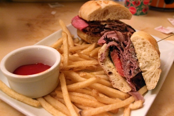 a roast beef sandwich with fries on a plate with a cup of ketchup