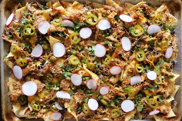 A tray of duck carnitas nachos with sliced radishes and jalapenos.