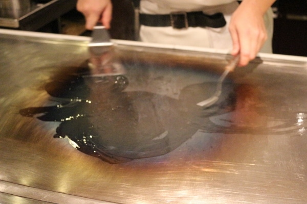 a hibachi chef\'s hands making a Mickey out of oil on the hot surface