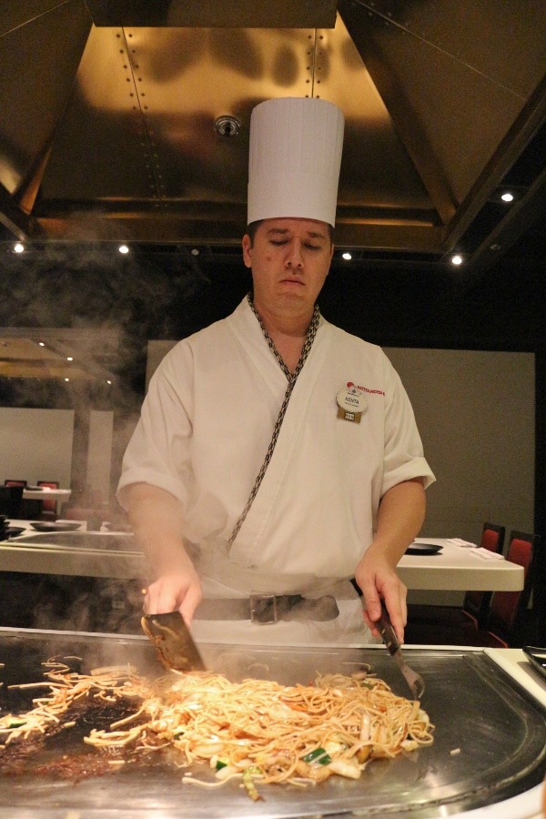 A chef cooking noodles on a hot surface