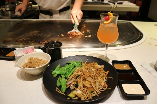 A plate of noodles with vegetables, a bowl of rice, and a drink