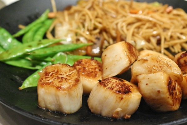 seared scallops on a plate with noodles and snow peas in the background