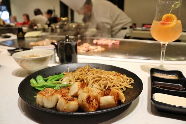 A plate of scallops with noodles, and a hibachi chef in the background
