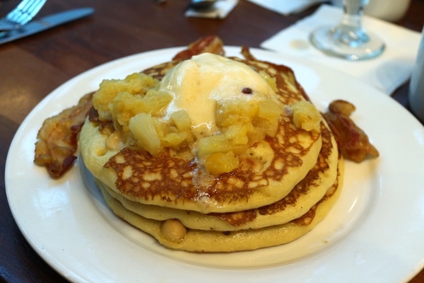 A stack of pancakes on a plate with pineapple and butter on top