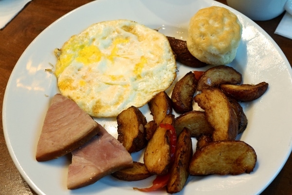 A plate of egg, breakfast potatoes, ham, and a small biscuit