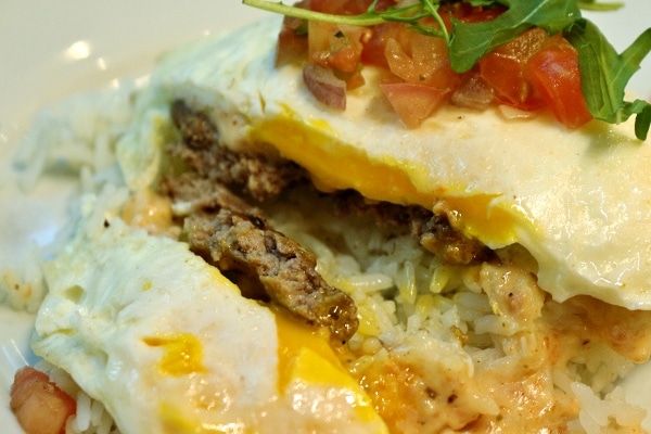 A closeup of a half-eaten loco moco showing a burger patty underneath a fried egg