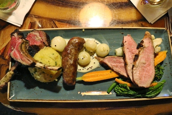 a platter of food including lamb chops, sausage, and pork tenderloin