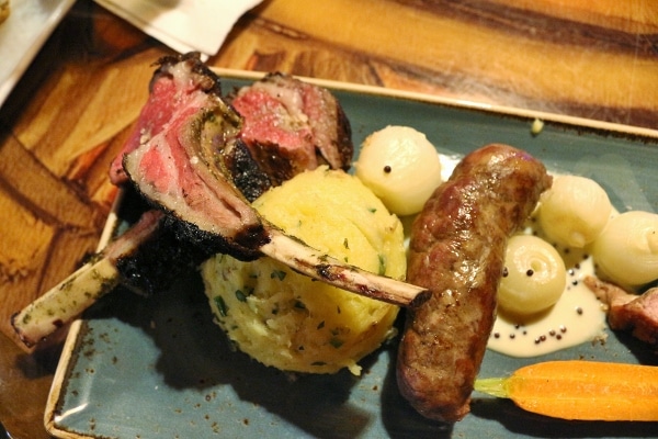 a closeup of lamb chops and African sausage served with a scoop of mashed potato