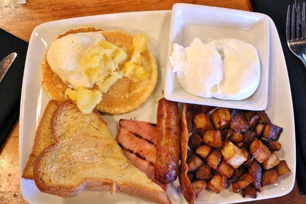 overhead view of a plate of eggs, home fries, breakfast meats, toast, and pancake