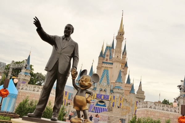 a statue of Walt Disney and Mickey Mouse in front of Cinderella\'s Castle