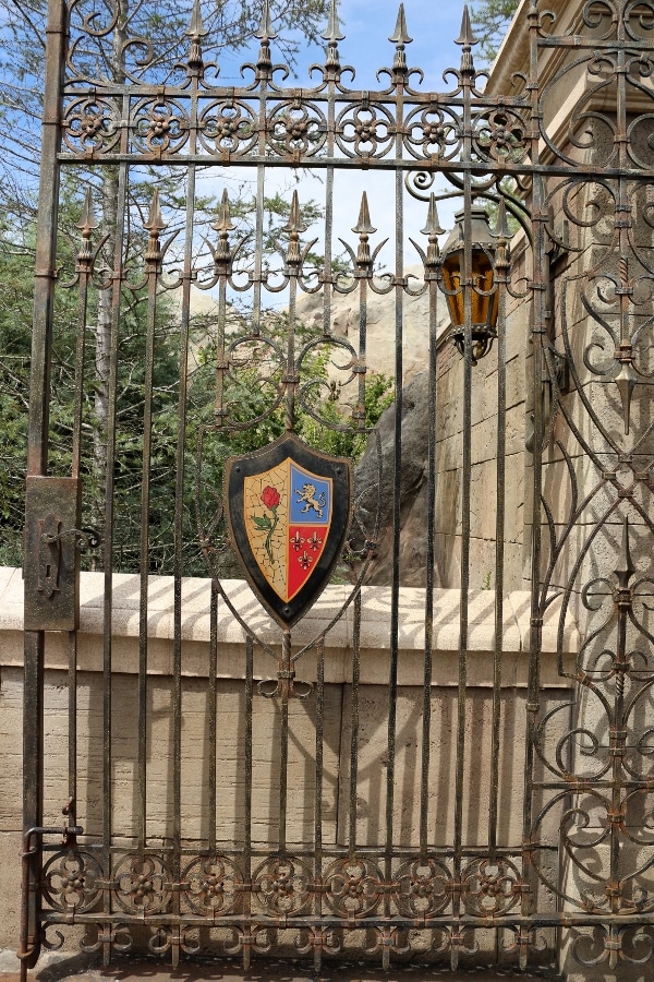 a metal gate with a Beauty and the Beast style coat of arms on it