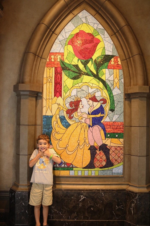 A boy standing in front of a Beauty and the Beast mural